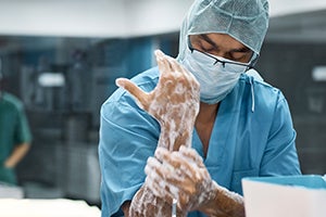 Coronavirus COVID-19 Protecting Health Care Workers stock. A clinician in scrubs and a mask washing his hands.