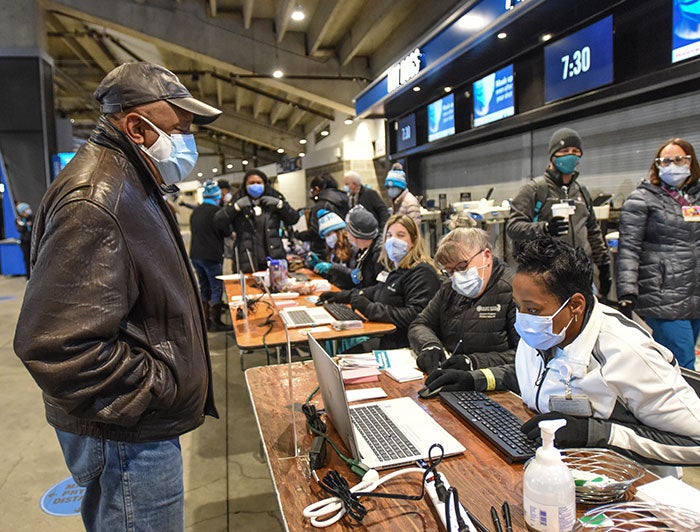 Older Black man wearing medical mask checks in at stadium with health workers