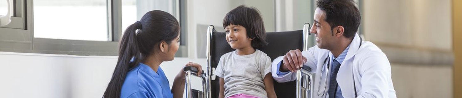 Little girl in a wheelchair with medical staff talking with her while kneeling down