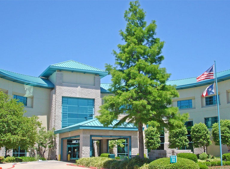 Titus Regional Medical Center exterior shpws beigh brick building with green trim on a sunny day, american and Texas flags flying from a flag pole